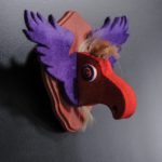 Trophy resembles a moose trophy, but is made from felt and wood. Moose head is orange wool and it has wings or ears that are lilac.